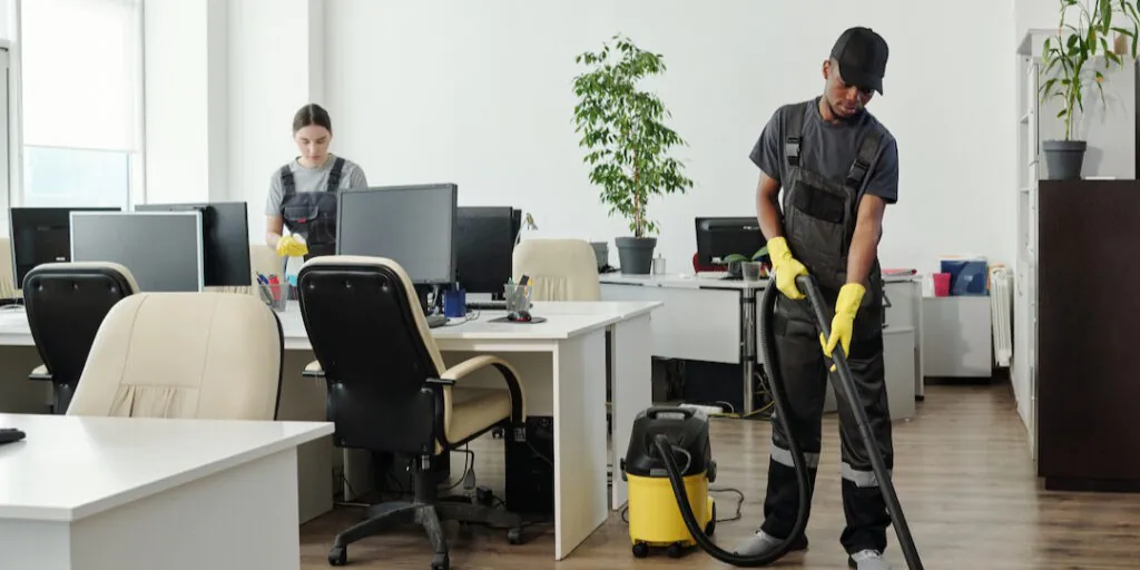 Cleaner vacuuming carpet in an office.