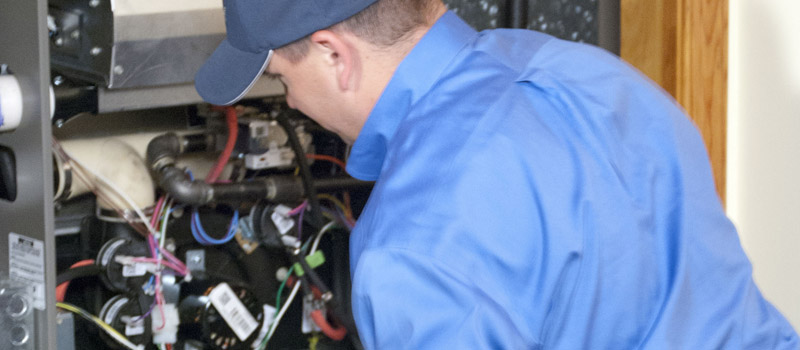 An HVAC technician examines components inside an open furnace unit.